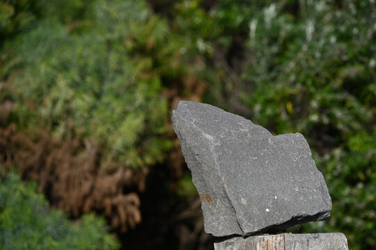 Large Stone With Pointy Edges Sitting Precariously Atop A Wooden Post, With Out Of Focus Greenery In The Background