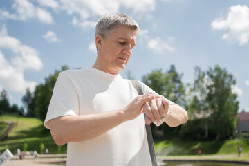 A retired man uses a fitness tracker bracelet smartwatch on his arm. Gray hair active exercises fitness training