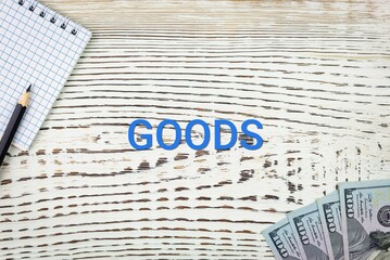 Naklejka premium GOODS - word (text) and dollars on a white wooden table, notebook, notepad. Business concept: buying, selling, commerce (copy space).