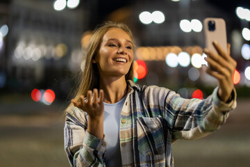 An attractive young woman using a smartphone for video call outside in the city at night