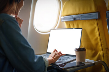 An Asian woman sits in a window seat in Economy Class using a white screen laptop computer that can use text or advertising while in flying. Travel, vacation