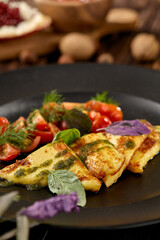 Grilled halloumi cheese with pesto sauce and tomatoes on black plate. Appetizer from fried cheese in greek style on wooden background. Hot appetizer of halloumi cheese in rustic style.