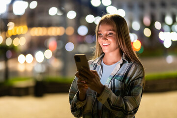 Outdoor portrait of beautiful young woman using her mobile phone at night.