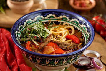 Eastern food - soup shourpa with vegetables and lamb meat on wooden table. Traditional uzbek soup with lamb meat, sweet pepper, tomatoes in rustic style. Caucasian cuisine on dark wooden background.