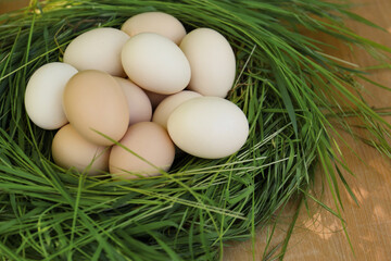 Nest made of green grass with fresh raw eggs on wooden table, closeup