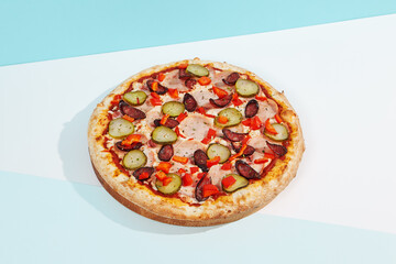 Italian pizza with sausage, jalapeno, ham and paprika on coloured background. Spicy pizza with jalapeno in minimal style on blue and orange color. American pizza delivery concept with color backdrop.