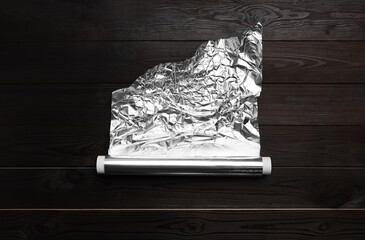 Roll of aluminum foil on dark wooden table, top view
