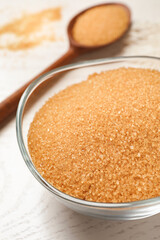 Brown sugar in bowl on white wooden table, closeup