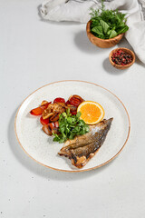 Fish dish - roasted dorado fillet with vegetables. Grilled fish fillet and roasted paprika, tomatoes and onion. Roast dorado fillet with garnish, greens and lemon on ceramic plate.