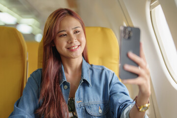 Attractive portrait of Asian woman sitting at window seat in economy class using mobile phone during inflight, travel concept, vacation, relax