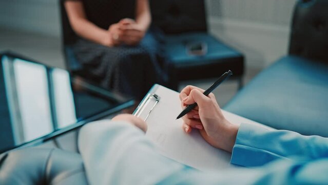 close up psychotherapist holding clipboard writing notes during consulting session meeting in the office