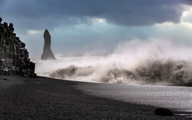 Reynisdrangar basalt rock columns standing in a stormy sea off the coast of Iceland. The formations here are also known as the Troll toes, due to Icelandic myth. The beach has black volcanic sand.