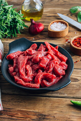 Raw uncooked beef meat sliced in strips with Ingredients for beef stroganoff over rustic wooden background.