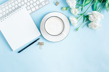 Flat lay of home office workspace with modern keyboard, cup of coffee and eustoma flowers on light blue background.