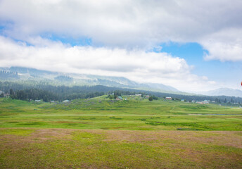 Panorama of beautiful countryside of India. sunny afternoon. wonderful springtime landscape in mountains. grassy field and rolling hills. rural scenery of Gulmarg. Jammu and Kashmir.