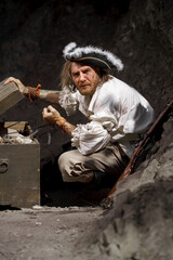Sea robber captain of pirate ship armed with treasure chest in cave. Concept historical halloween. Filibuster cosplay