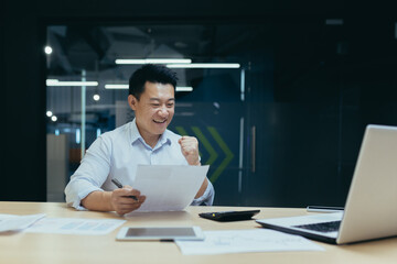 Fototapeta na wymiar Successful and confident asian businessman reading bank letter and financial report, happy and celebrating triumph success, holding hand up