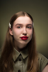 Portrait of a young attractive girl with a smooth hairstyle and clips on her blonde hair in a stylish green dress with expressive red lips. Close-up, green background