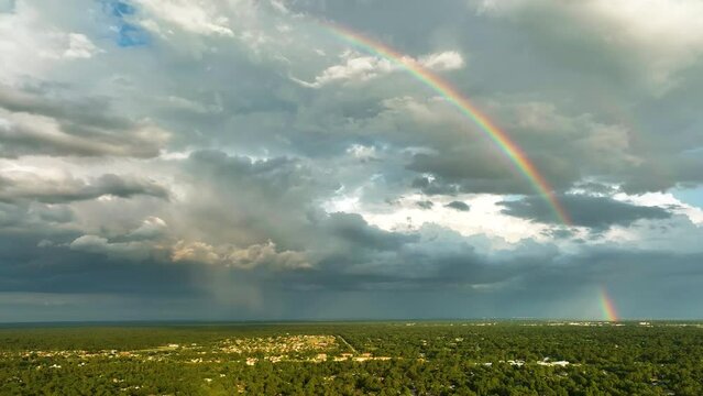 Colorful rainbow against landscape of dark ominous clouds forming on stormy sky before heavy thunderstorm over rural town area