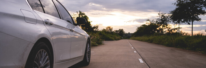 Behind a beautiful white car parked on a road with beautiful sunsets. with space for text.