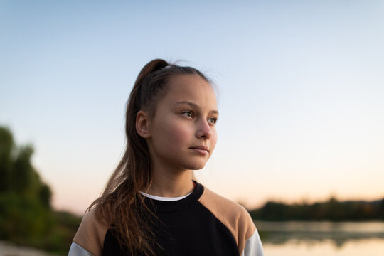 Portrait of beautiful preteen girl against river and forest in autumn outdoors