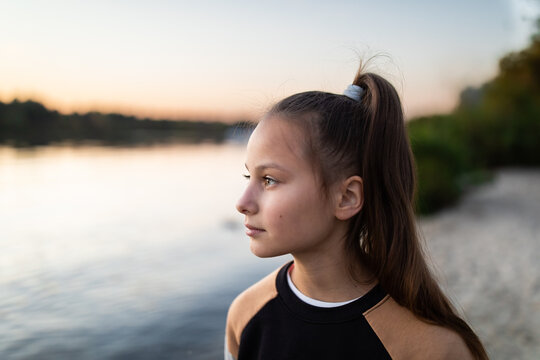 Portrait of beautiful preteen girl against river, beach and forest in autumn outdoors