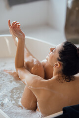 Young woman hugs her legs while sitting in the bath - 516160347