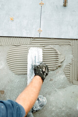 close up of worker hand plastering, adding adhesive with comb trowel