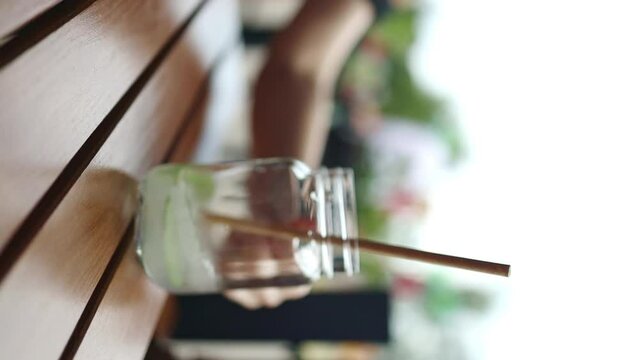 Cold summer mojito cocktail in a glass. Woman hand takes a glass of tropical drink mojito with eco straws