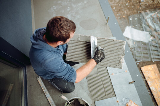 industrial worker, handyman installing ceramic tiles on balcony floor. Balcony area covered in ceramic tiles with strong adhesive