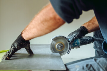 professional caucasian construction worker cutting ceramic tiles with angle grinder during tiling...