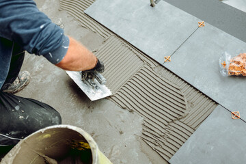 Professional construction worker, tiler laying adhesive and placing ceramic tiles on waterproof...