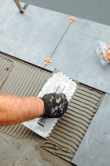 hand of professional construction worker, tiler laying adhesive and placing ceramic tiles on...