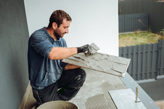Professional construction worker, tiler laying adhesive and placing ceramic tiles on balcony floor. Details of home renovation, construction works