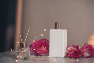 Fototapeta na wymiar Liquid home fragrance in glass bottle with bamboo sticks and rose flowers with white jar of perfume on marble table close up. Healthy beauty treatment.