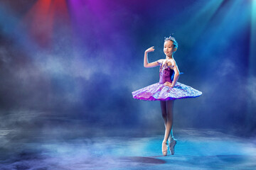 Fototapeta na wymiar A little Japanese ballerina dances on stage in a lilac tutu on pointe shoes classical ballet.