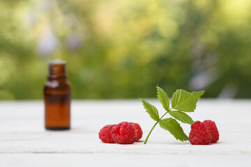 Red Raspberry (rubus idaeus) seed oil bottle with red raspberry and leave on white wooden and...