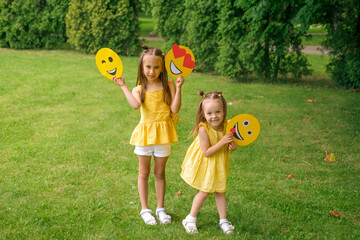 Winking, in love and tired, showing the tongue of a cardboard emoji in the hands of children