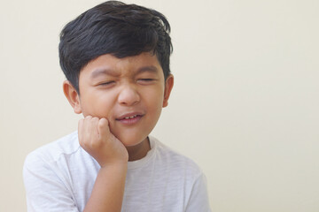 Little Asian boy 5 year old suffering from toothache pain while eating candy, holding his cheek, dental pain and he feel so sad. 