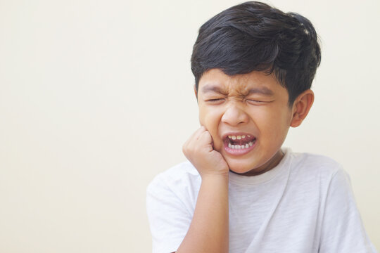 Little Asian Boy 5 Year Old Suffering From Toothache Pain While Eating Candy, Holding His Cheek, Dental Pain And He Feel So Sad. 