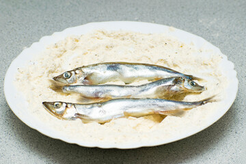 the process of cooking capelin in the oven. fish lying in a plate with flour.