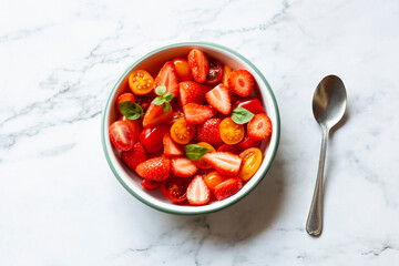 Portion of strawberry and tomato cherry salad decorated with basil leaves