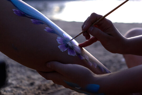 Hand of an artist painting the body of a woman during sunset on a beach