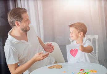 father's day, the son makes a gift to his father for the holiday. Happy family adult parent dad and small son having fun at home 