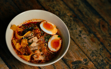 Tom yum or spicy noodle served with boiled eggs and crispy pork,wooden background