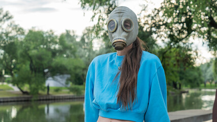 Girl with long hair in a gas mask on the river bank. Alienation in the city. Fashion, ecology and...