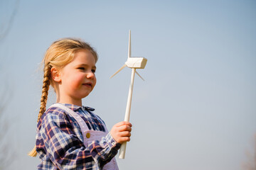 Child playing and looks interested at a wind turbine toy - Concept of future generation and...