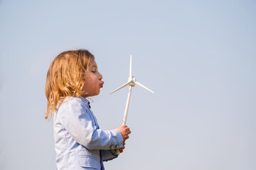 Closeup of little boy blowing a wind turbine toy and studying how green energy works from a young...