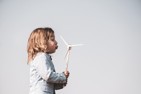 Closeup of little boy blowing a wind turbine toy and studying how green energy works from a young age - Concept of future generation and enewable Energy