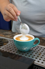 The barista is pouring milk into a coffee mug.